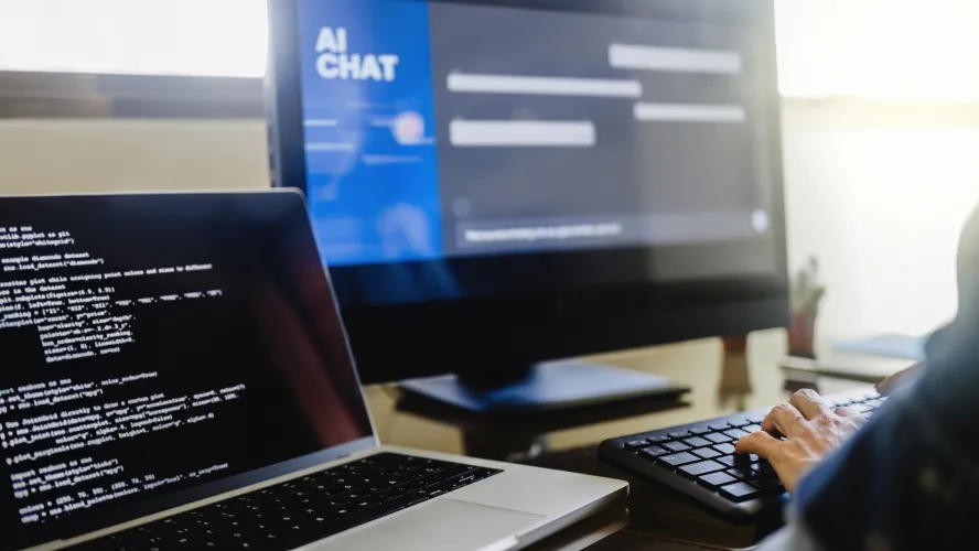 Person typing on keyboard with laptops showing AI chat interface