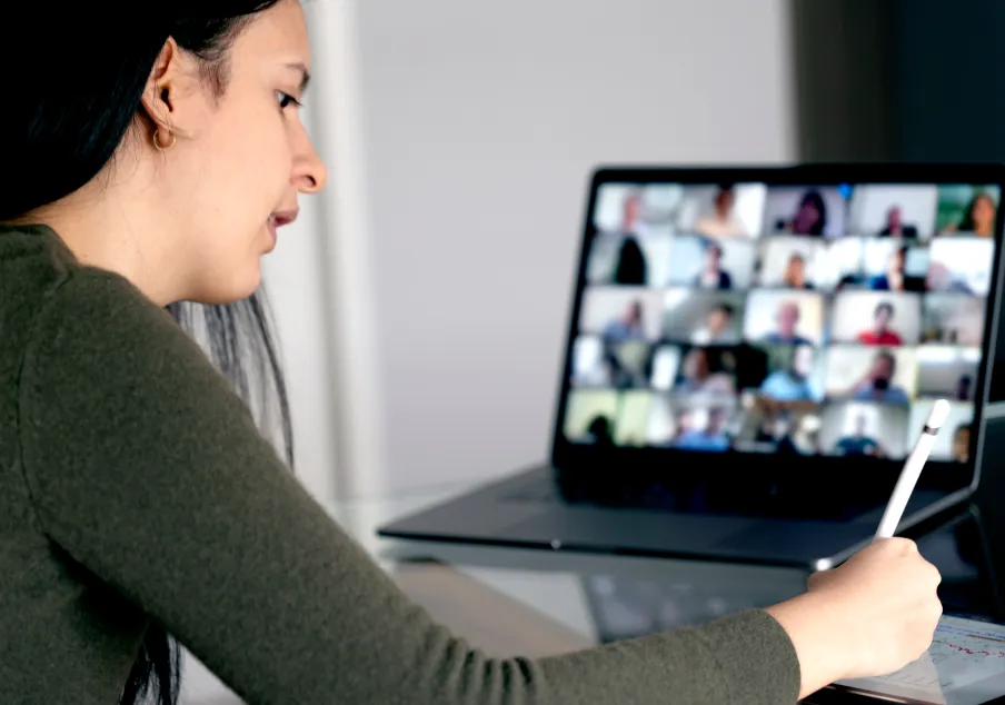 Woman participating in virtual meeting and taking notes
