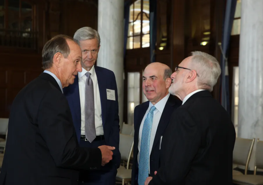 Four men in suits conversing inside formal meeting room
